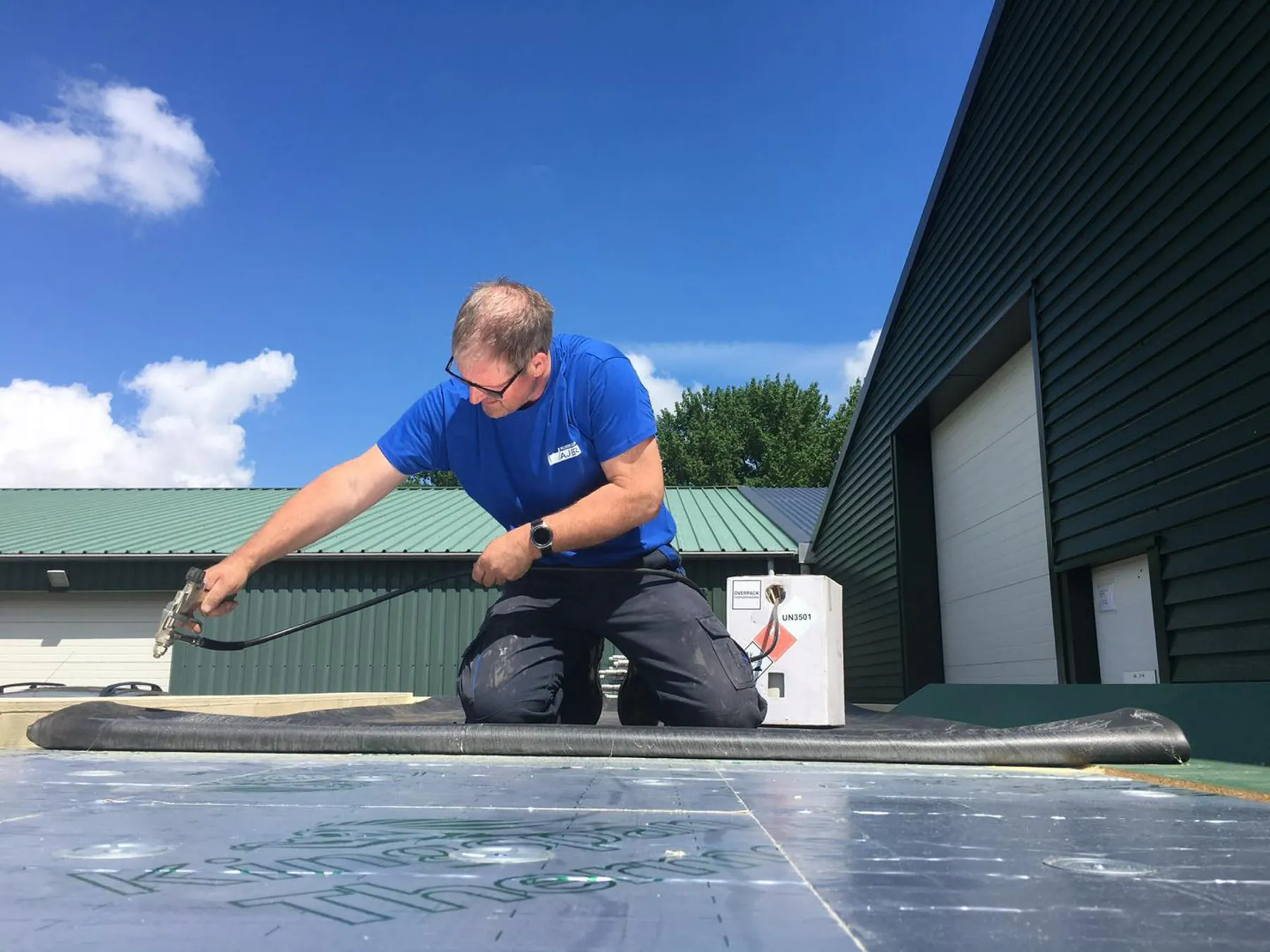 Vakman van Klusbedrijf Wajer werkt aan een dak onder een blauwe lucht